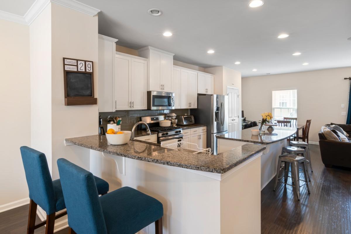 Bright open-plan kitchen with white cabinets, granite countertops, a central island with bar stools, and stainless steel appliances in a modern family home.
