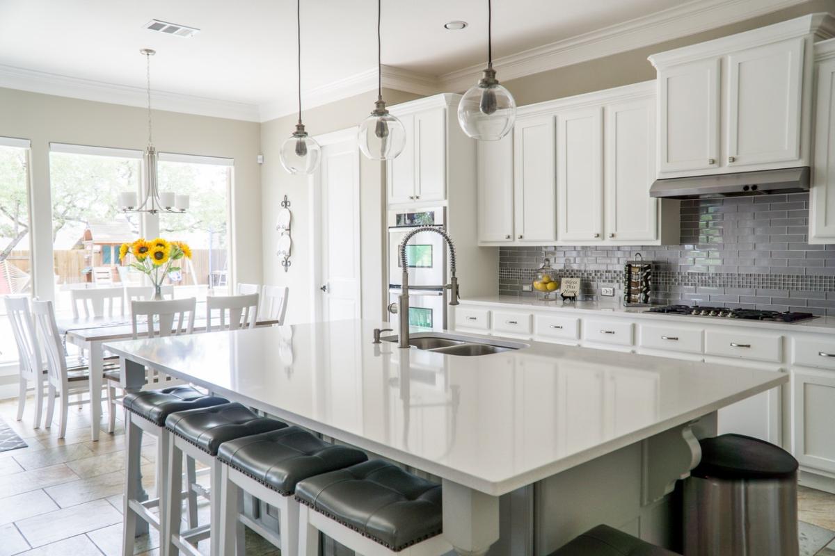 Bright, modern kitchen with white cabinetry, a large island with seating, pendant lighting, and an open dining area filled with natural light.