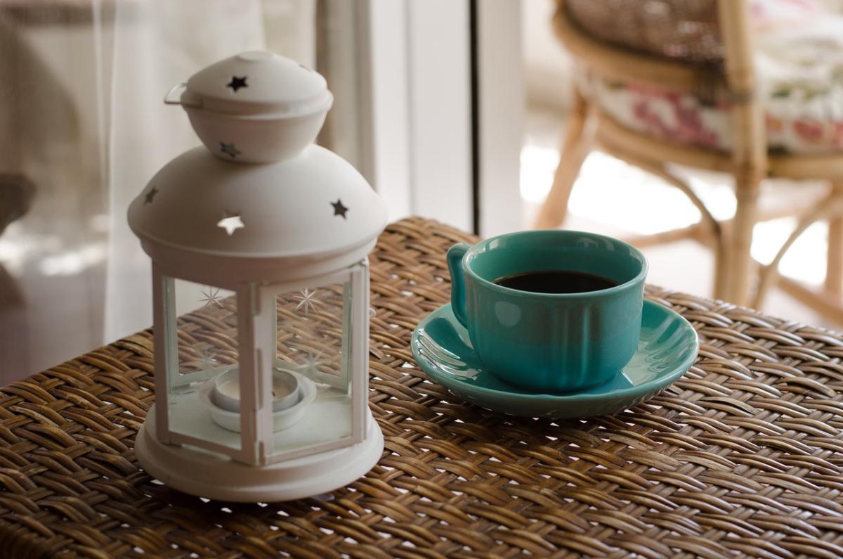 Turquoise cup of coffee on a woven rattan table beside a white decorative lantern in a cosy indoor setting.