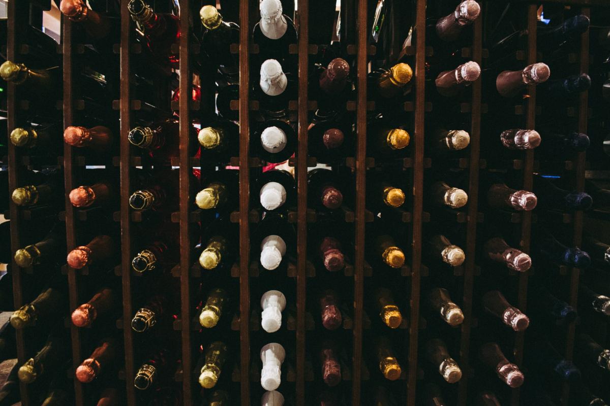 Wine bottles stored horizontally in a wooden wine rack, showing a variety of bottle tops arranged in neat rows.