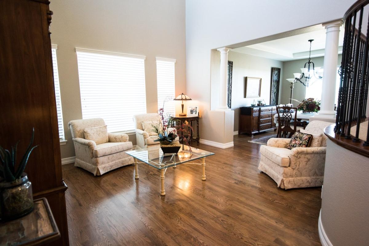 Spacious living room with wooden floors, upholstered armchairs, a glass coffee table, and an open layout leading to a dining area.