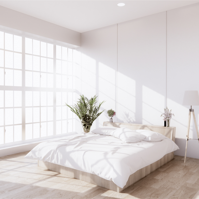 Bright, minimalist bedroom with a low wooden bed, white bedding, large grid windows, and natural light casting soft shadows.